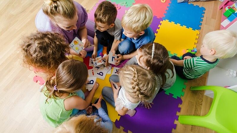 Mehrere Kinder sitzen gemeinsam im Kreis auf bunten Spielmatten.
