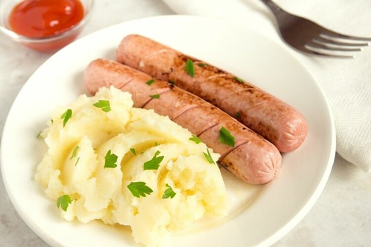 Teller mit Bratwürsten, Kartoffelpüree und Gemüse.