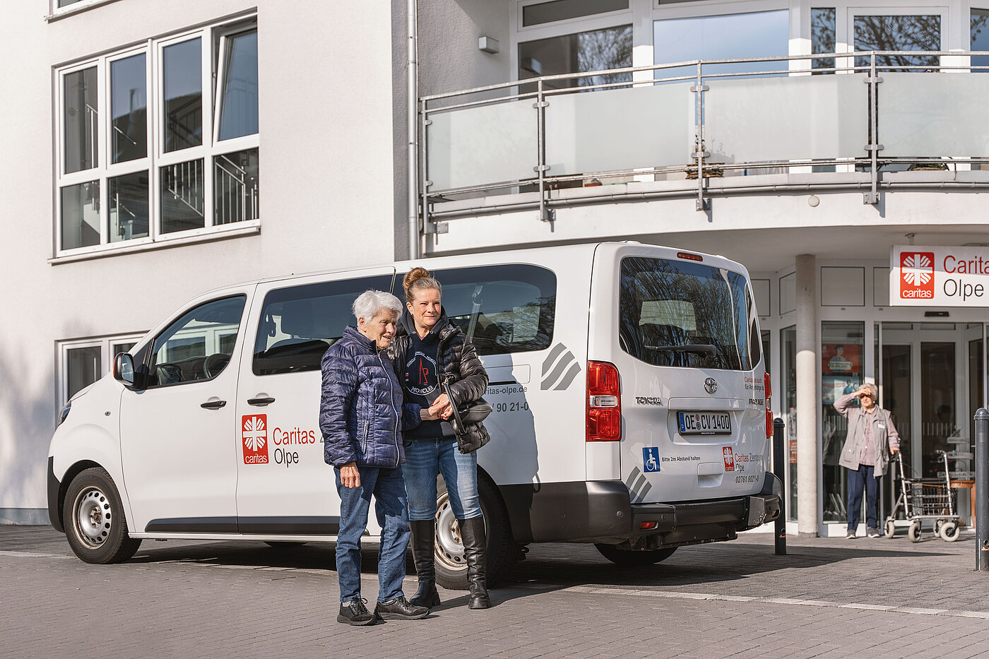 Zwei Frauen stehen vor einem weißen Caritas-Transporter vor dem Eingang der Caritas-Tagespflege Olpe