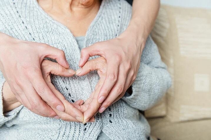Zwei Herzen aus Händen geformt vor einer sitzenden Seniorin