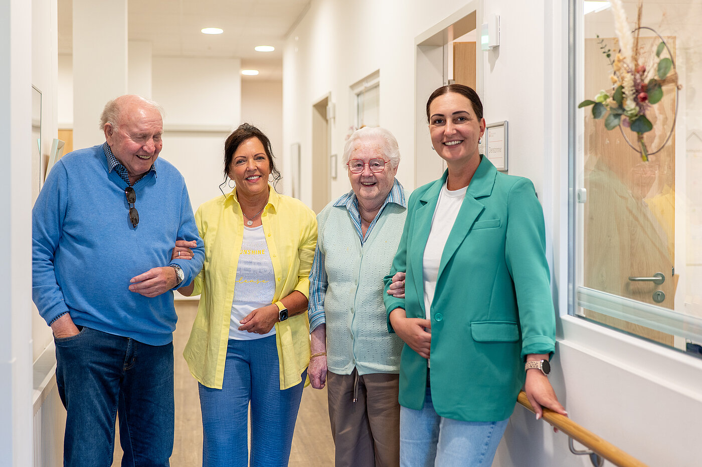 Gruppenbild: Ein männlicher Gast, eine Mitarbeiterin, ein weiblicher Gast und die Leiterin der Tagespflege stehen lächelnd nebeneinander.