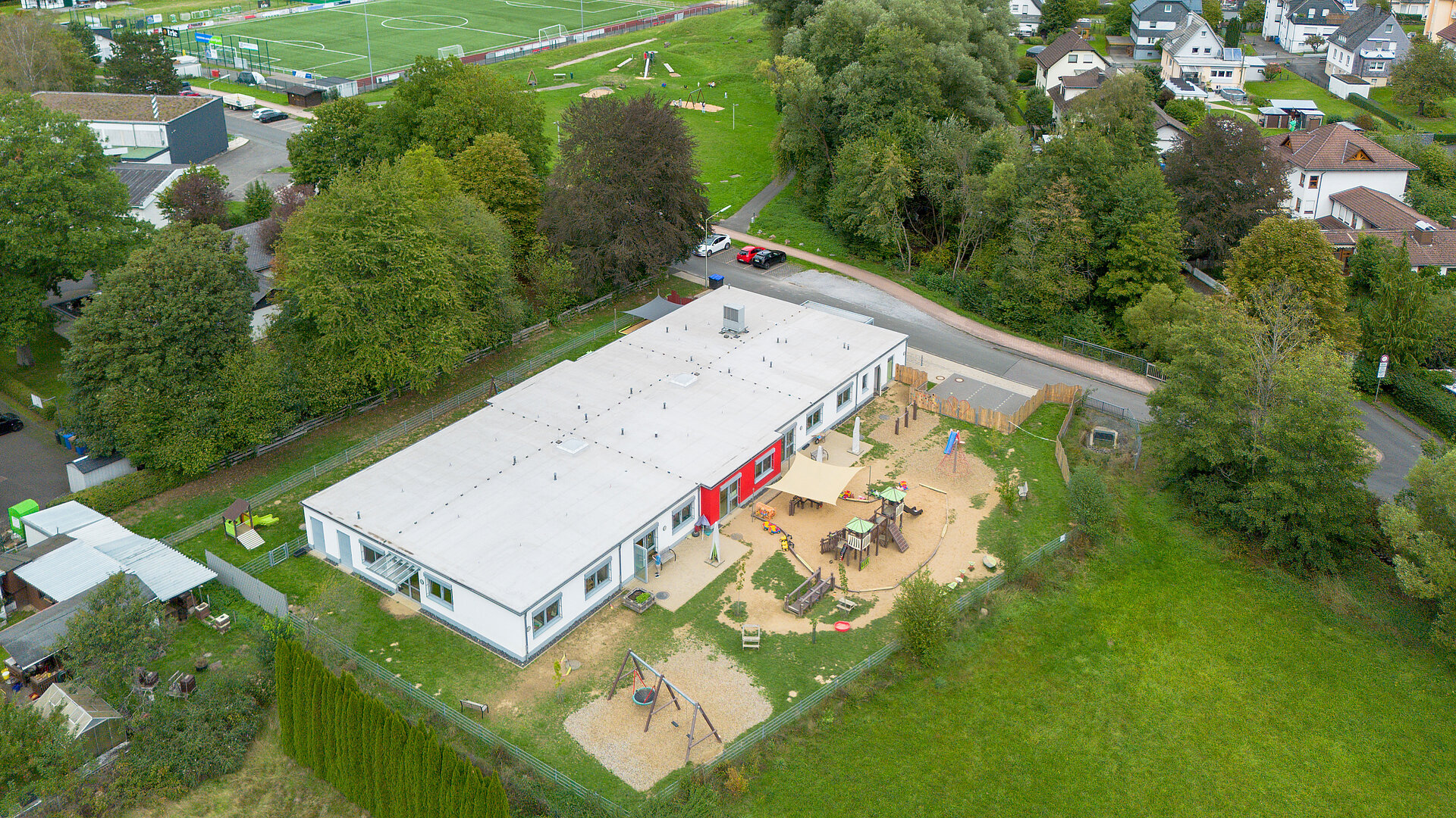 Luftaufnahme der Caritas-AufWind Kita in Niederdiel­fen mit Gebäude, Außenspielbereich und umliegender Landschaft