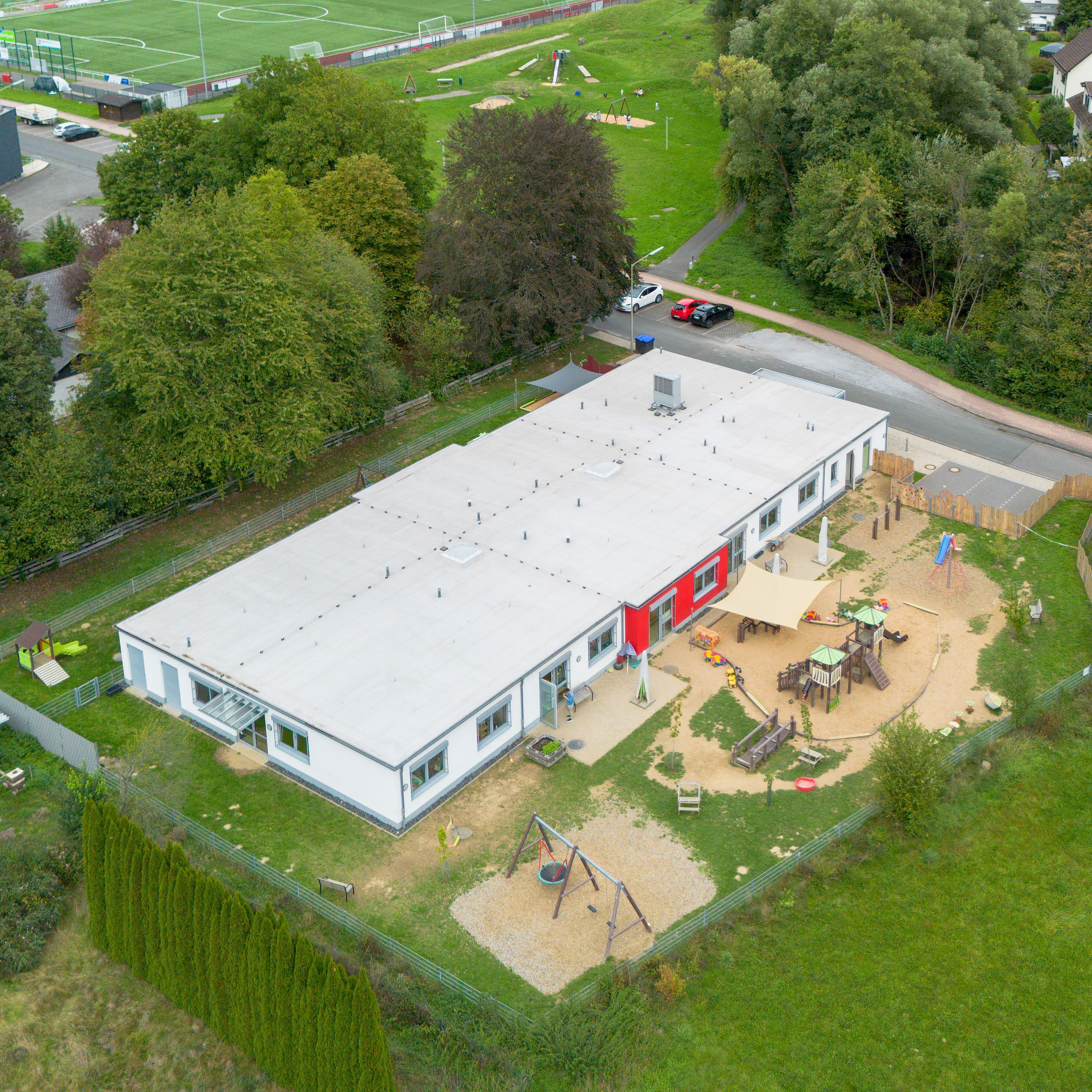 Luftaufnahme der Caritas-AufWind Kita in Niederdiel­fen mit Gebäude, Außenspielbereich und umliegender Landschaft