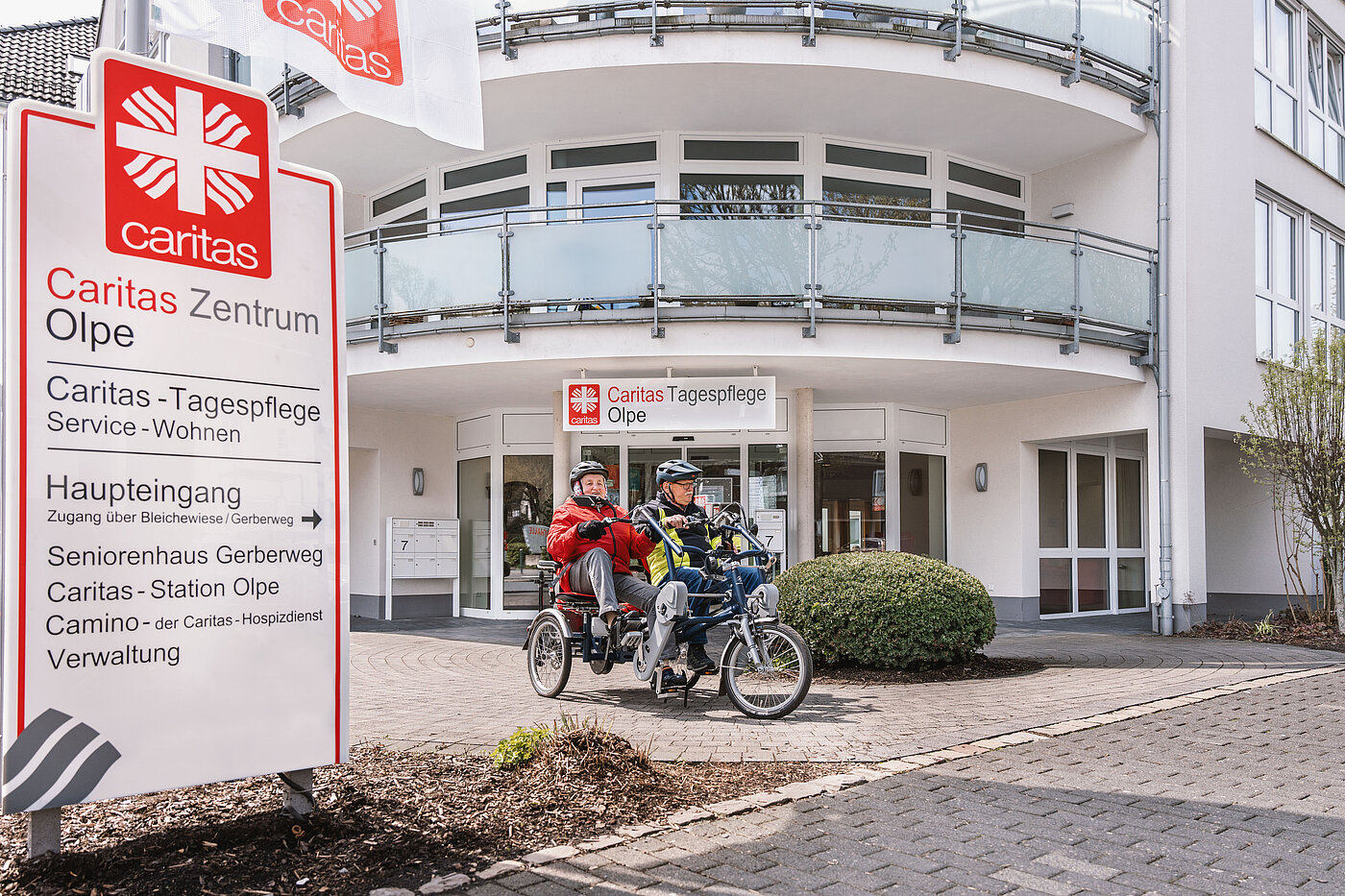 Eingangsbereich der Caritas-Tagespflege Olpe und zwei Personen auf einem Tandem