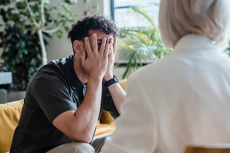Ein junger Mann, der in der Beratung die Hände vor dem Gesicht hält.