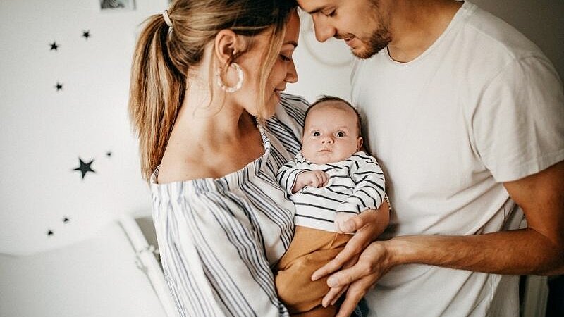 Eine Frau und ein Mann halten gemeinsam ein Baby auf dem Arm und schauen es an.