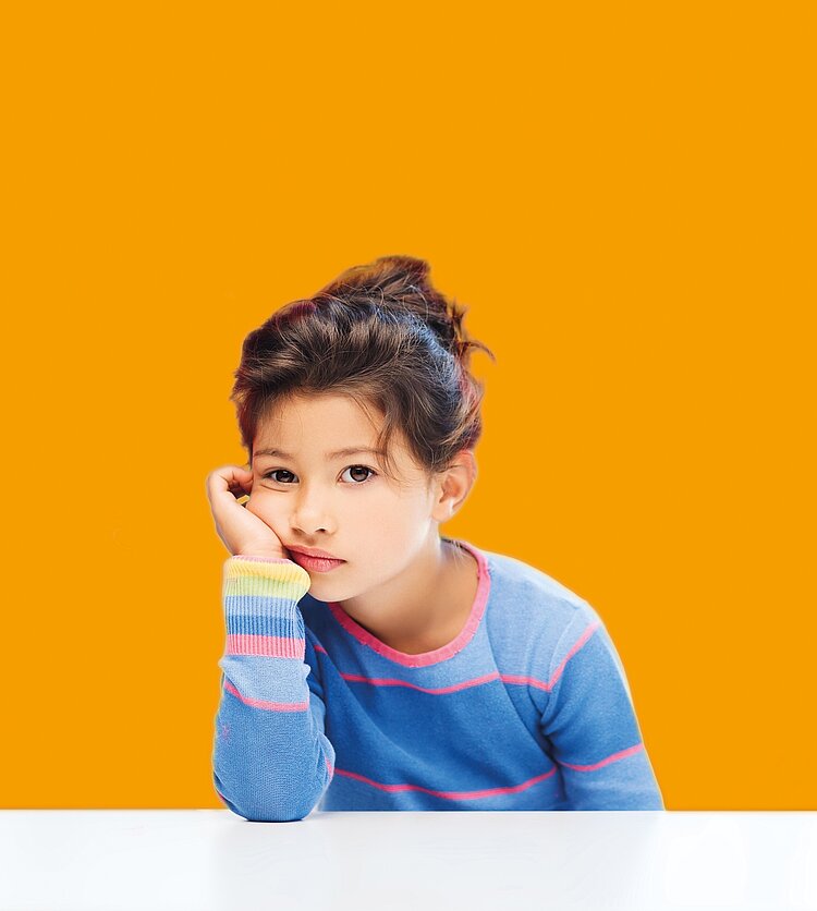 Ein Mädchen sitzt nachdenklich vor einem orangefarbenen Hintergrund.