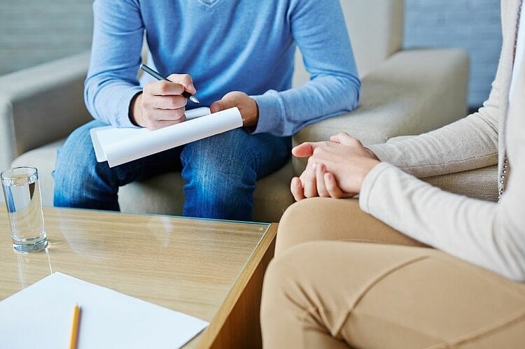 Zwei Personen sitzen sich in einem Beratungsgespräch gegenüber, eine Person macht Notizen.