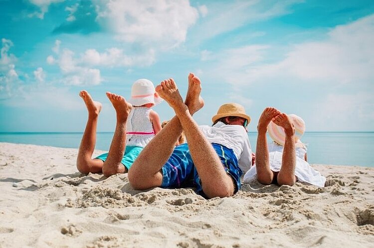 Mehrere Personen liegen am Strand und strecken ihre Beine in die Luft.