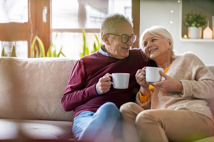 Älteres Paar sitzt auf dem Sofa und trinkt gemeinsam aus weißen Tassen