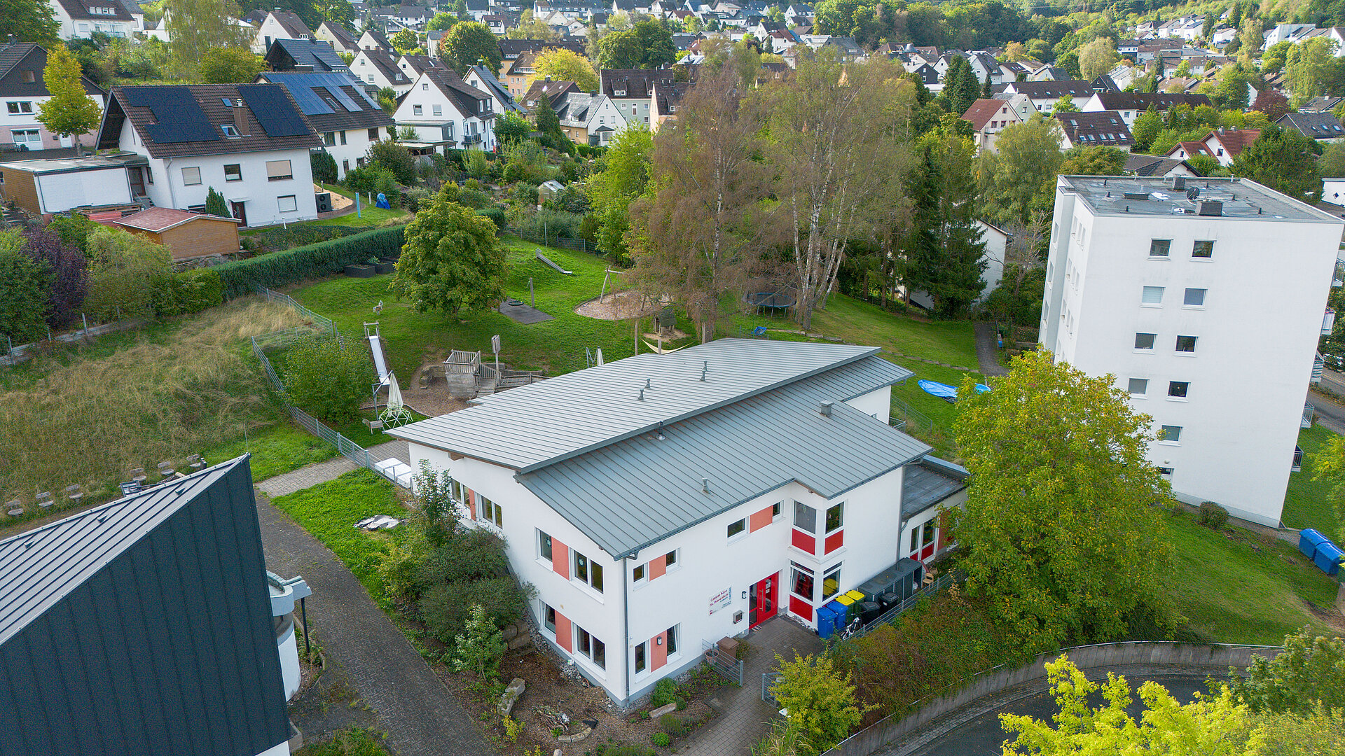 Luftaufnahme der Caritas-AufWind Kita in Burbach mit umliegenden Wohnhäusern und Grünflächen