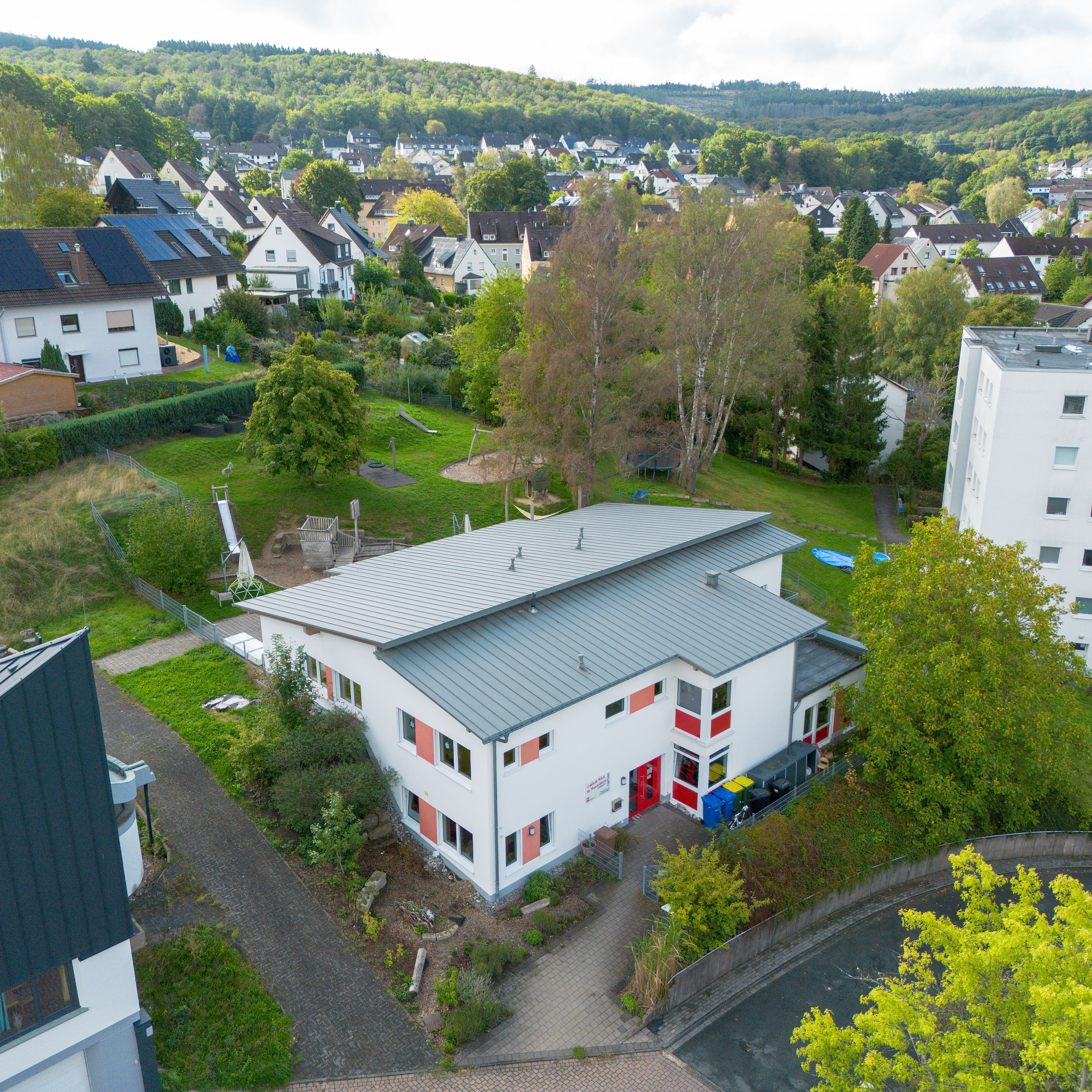 Luftaufnahme der Caritas-AufWind Kita in Burbach mit umliegenden Wohnhäusern und Grünflächen