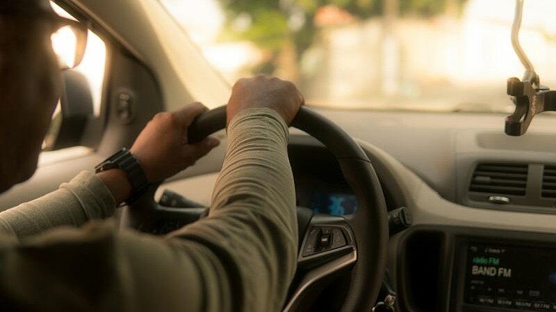 Ein Mann sitzt am Steuer eines Autos und hält während der Fahrt beide Hände am Lenkrad.