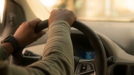Ein Mann sitzt am Steuer eines Autos und hält während der Fahrt beide Hände am Lenkrad.