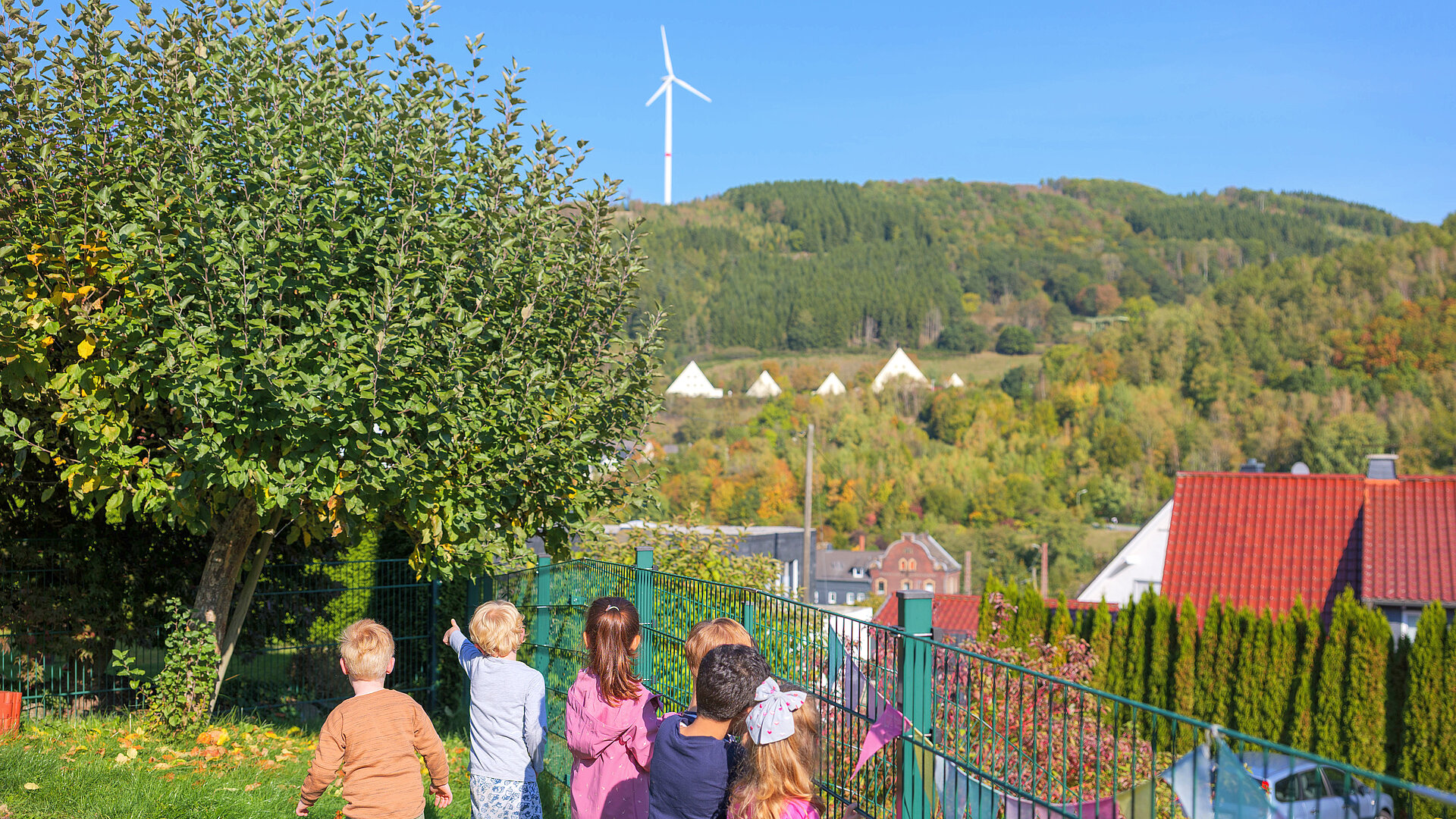 Kita-Kinder stehen am Zaun des Außengeländes und zeigen auf die Hügel des Sauerlands.